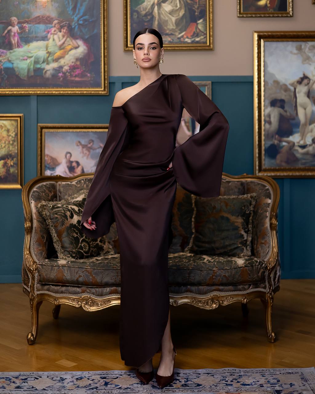 Woman in a dark brown dress standing in an ornate room with classical paintings on the wall.