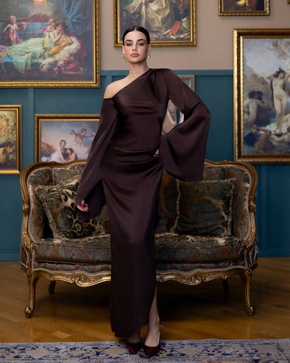 Woman in a dark brown dress standing in an ornate room with classical paintings on the wall.