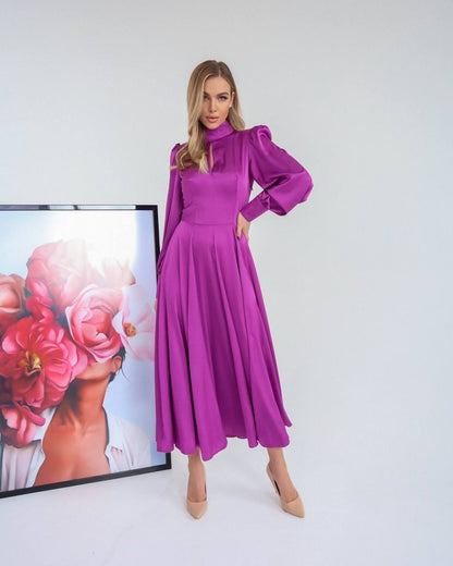 Woman wearing a purple dress standing in front of a floral painting on a white wall.