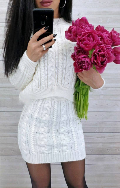 Person wearing a white cable knit dress holding pink flowers and taking a selfie.