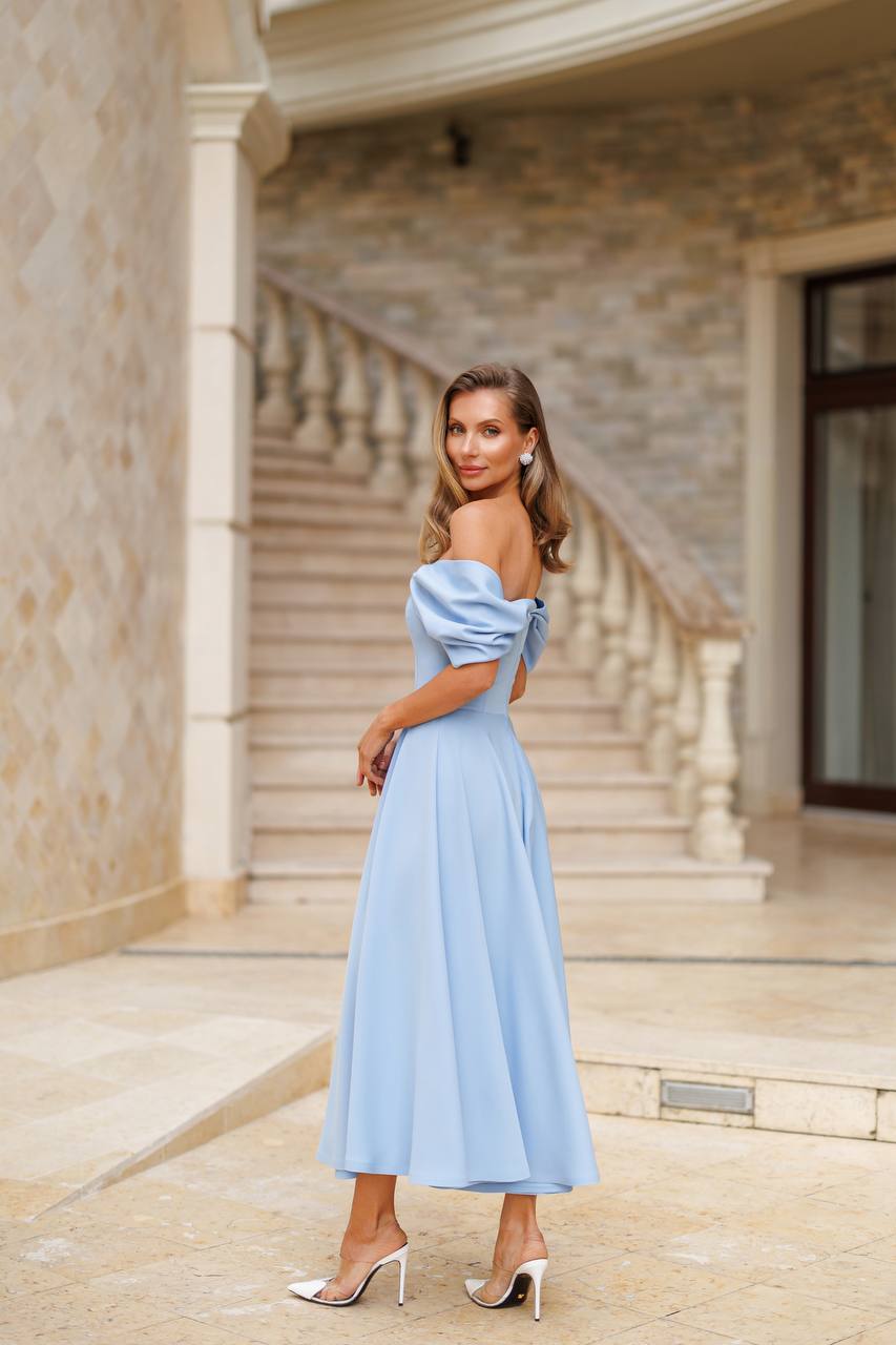 Woman in a light blue off-shoulder dress standing in front of a building with columns.