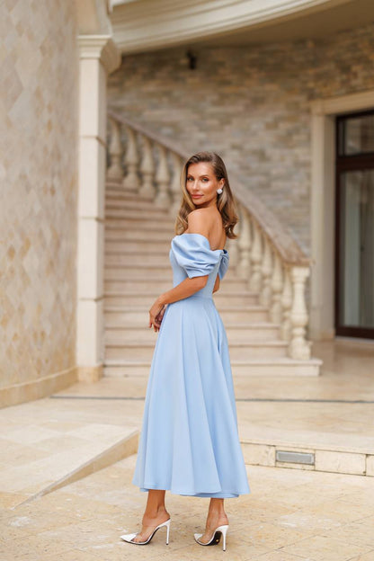Woman in a light blue off-shoulder dress standing in front of a building with columns.