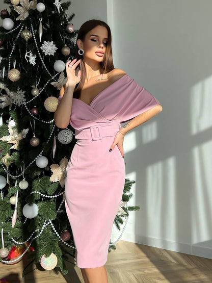 Woman in a pink dress standing next to a decorated Christmas tree indoors.
