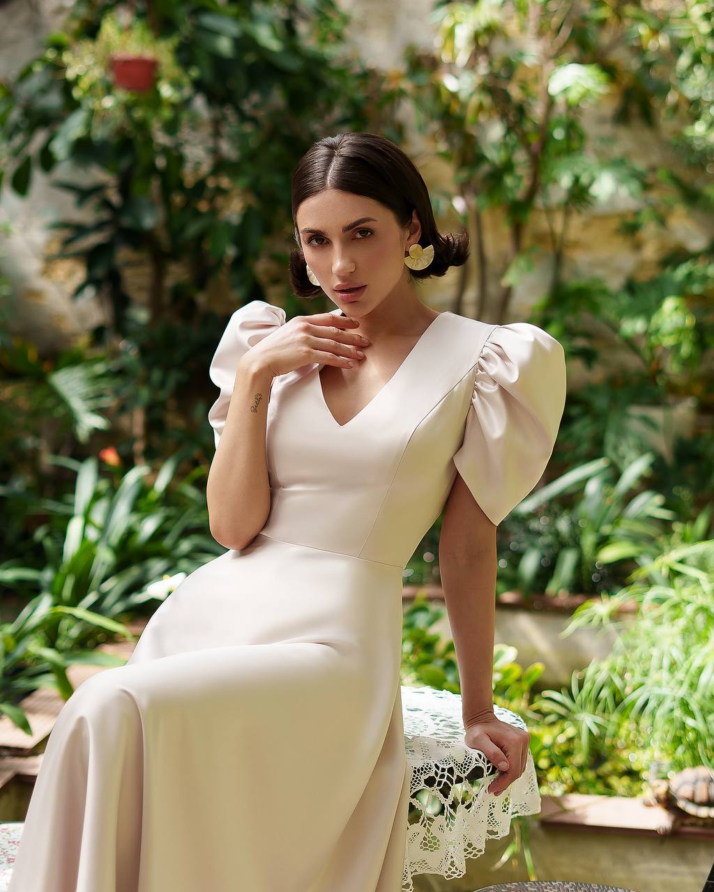 Woman in a white dress sitting outdoors with greenery in the background
