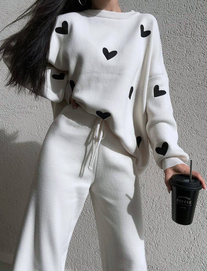 Person wearing a white sweater with black heart patterns against a plain background