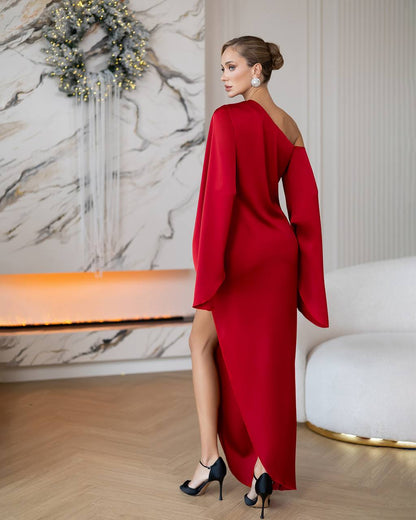 Woman in a red dress standing in a stylish room with marble wall and white sofa.