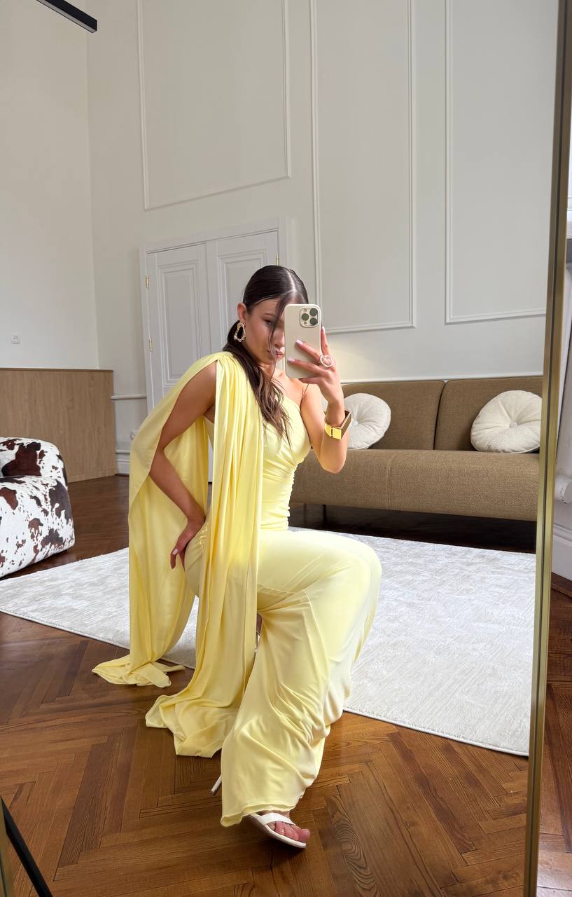 Woman in a yellow outfit taking a mirror selfie in a room with a couch and decorative pillows.