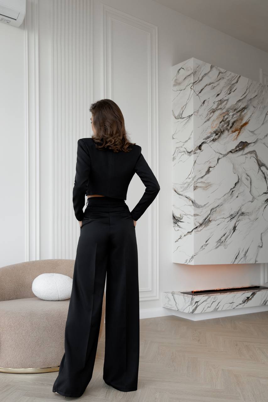 Person wearing a black outfit standing in a stylish room with marble wall art.