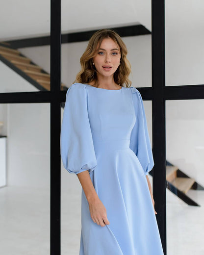 Woman wearing a light blue dress standing in a modern interior setting.