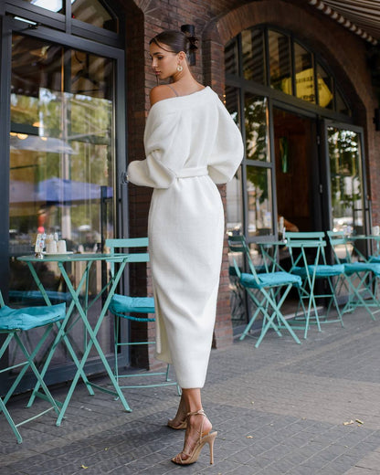 Woman in a white outfit standing outside a building with teal chairs and tables.