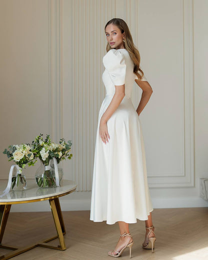 Woman in a white dress standing in a room with floral arrangements on a table.