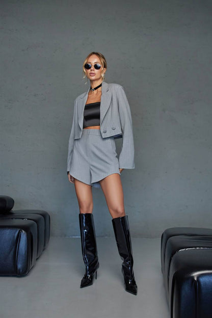 Woman in a gray outfit with black boots standing against a plain background
