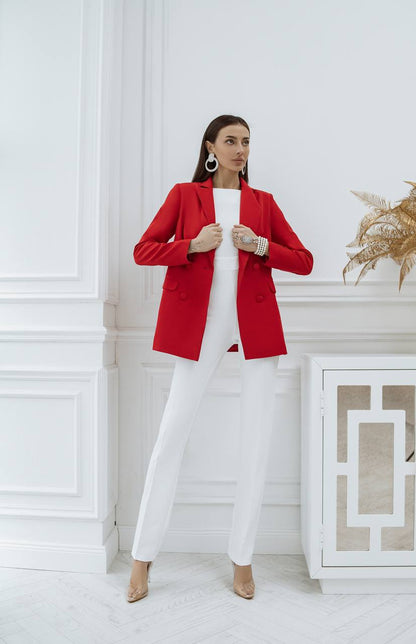 Woman wearing a red blazer over a white outfit in a stylish interior setting.