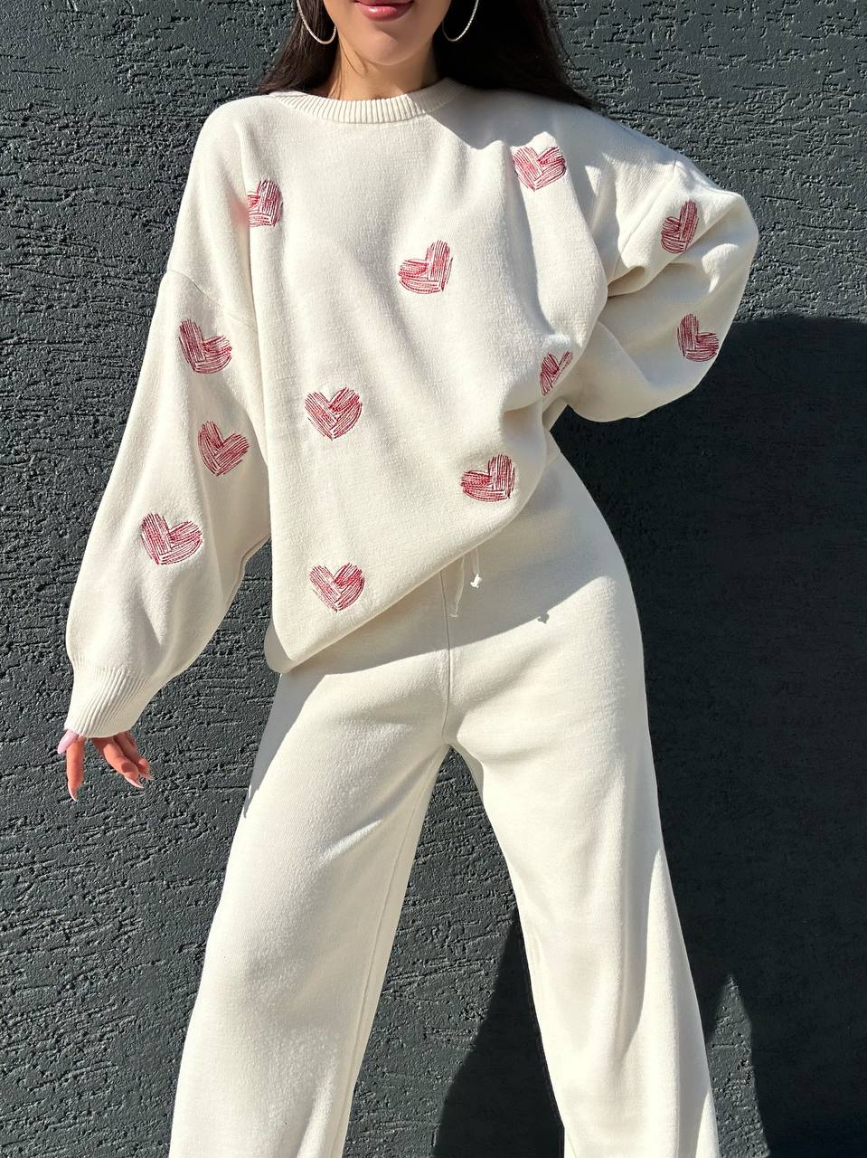 Person wearing a white sweater with pink heart patterns against a dark background
