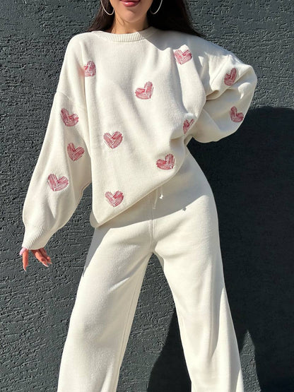 Person wearing a white sweater with pink heart patterns against a dark background