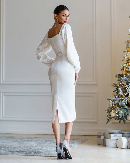 Woman in a white dress standing in a room with a decorated Christmas tree.