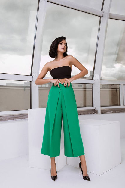 Woman wearing a black strapless top and green wide-leg pants in an indoor setting.