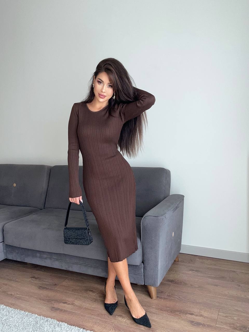Woman in a brown dress standing in a room with a gray couch.