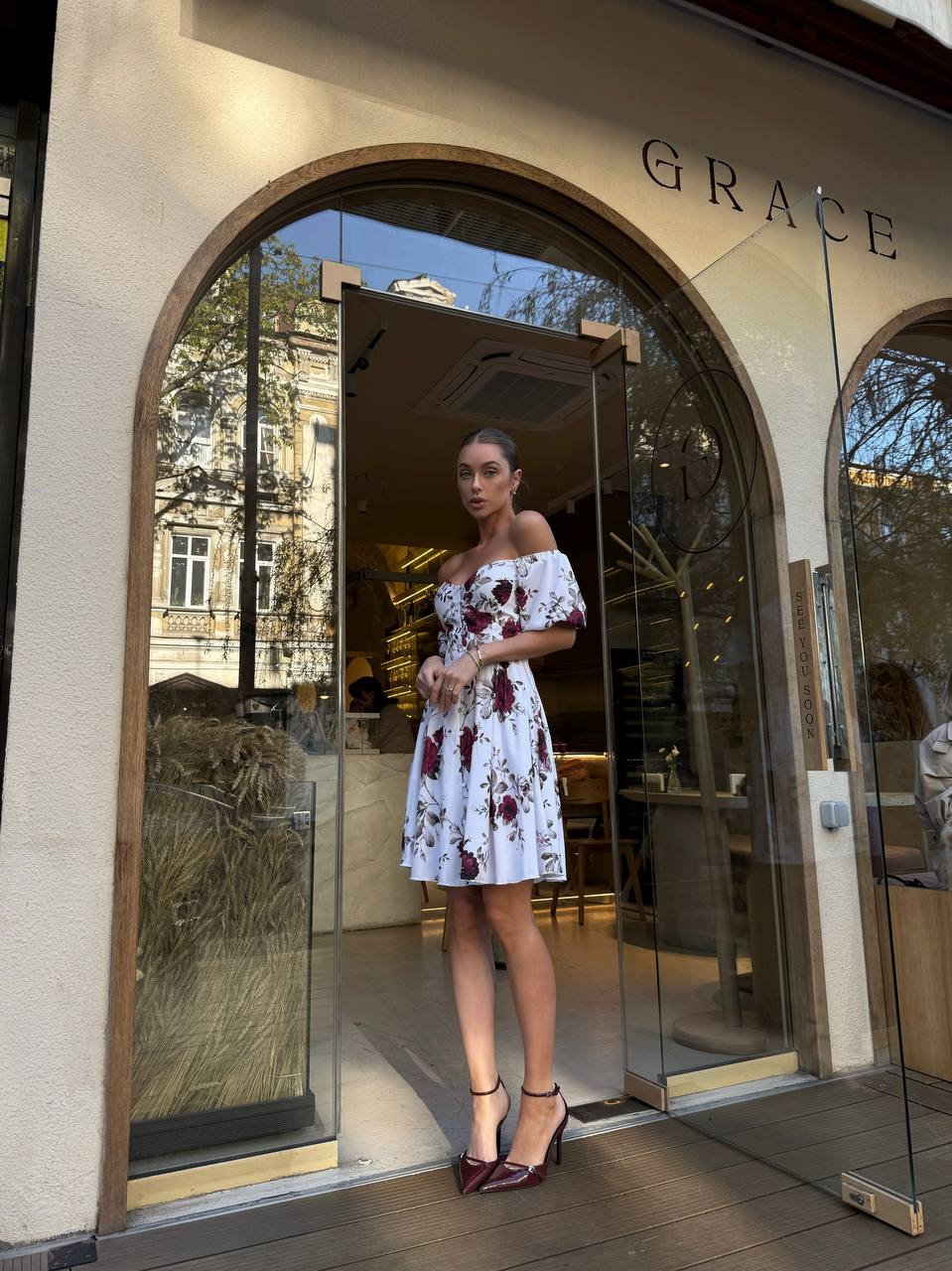 Woman in a floral dress standing outside a store named 'Grace'.