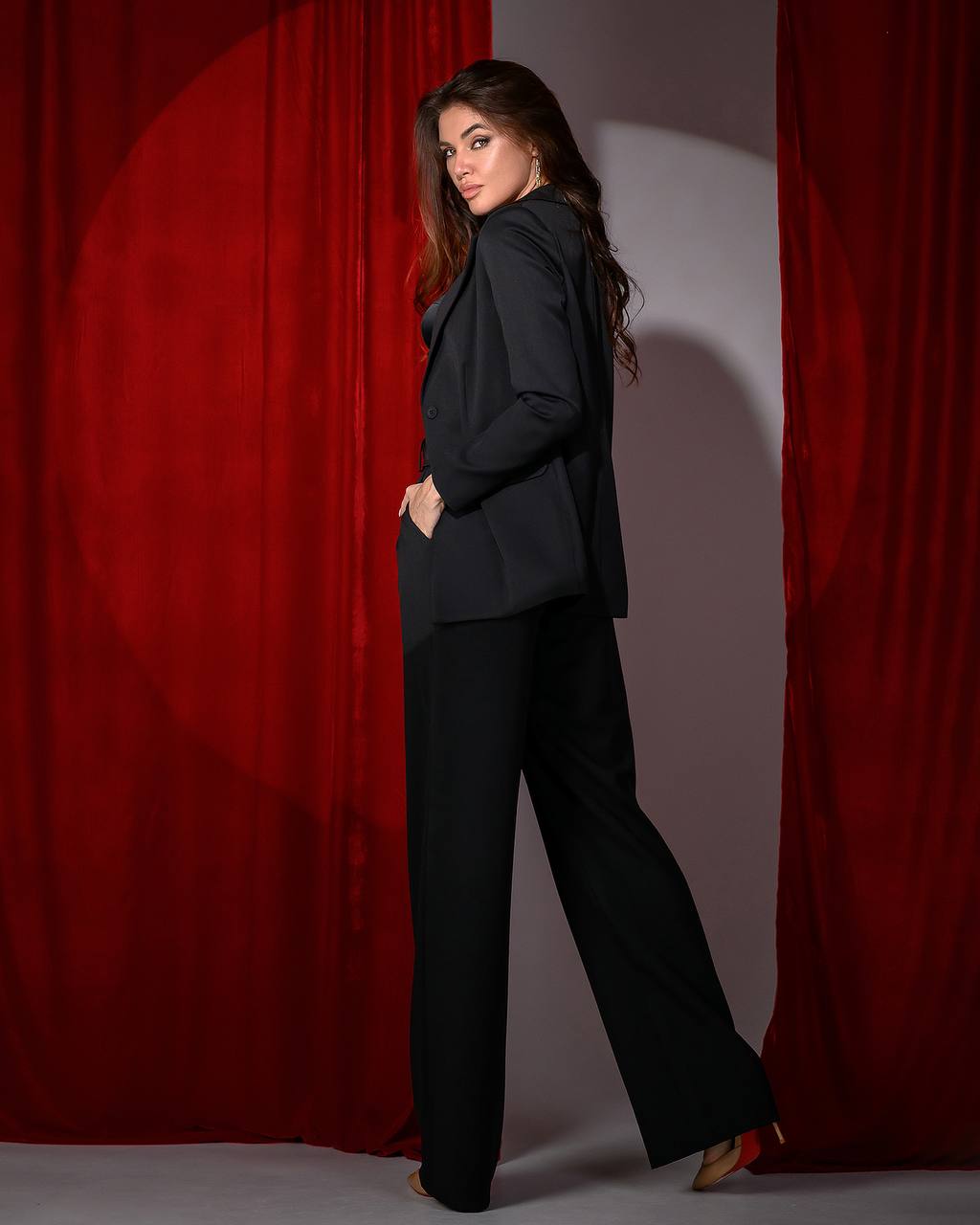 Woman in a black outfit standing against a red curtain backdrop