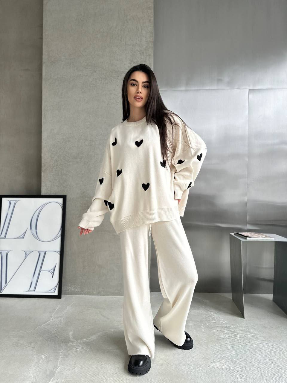 Woman wearing a white outfit with black heart patterns in a minimalistic room.