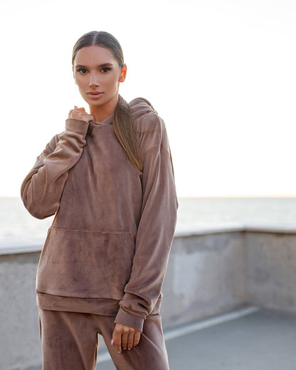 Woman wearing a brown hoodie and pants on a rooftop with a blurred background