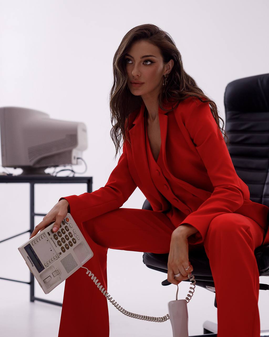 Woman in a red suit sitting on a chair holding an old-fashioned telephone.