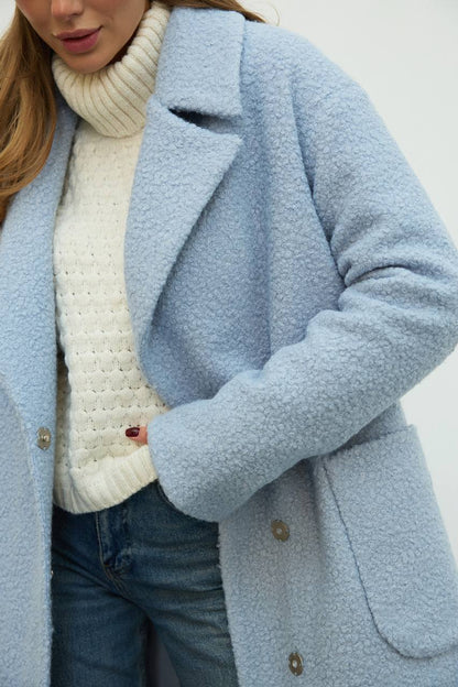 Light blue coat worn over a white sweater and jeans against a plain background