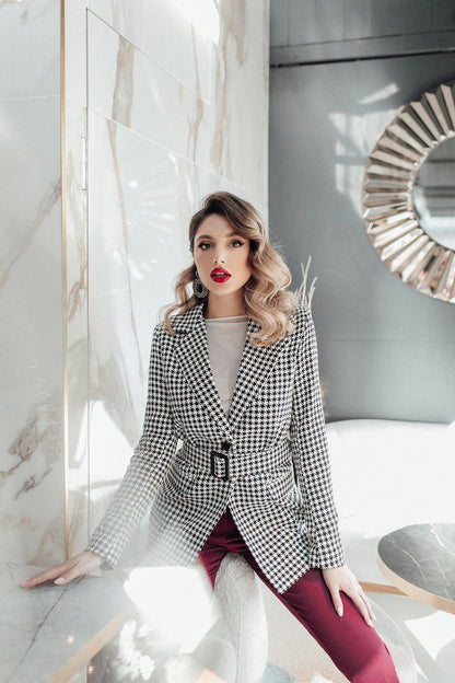 Woman in a checkered blazer and red pants posing in a modern interior setting.