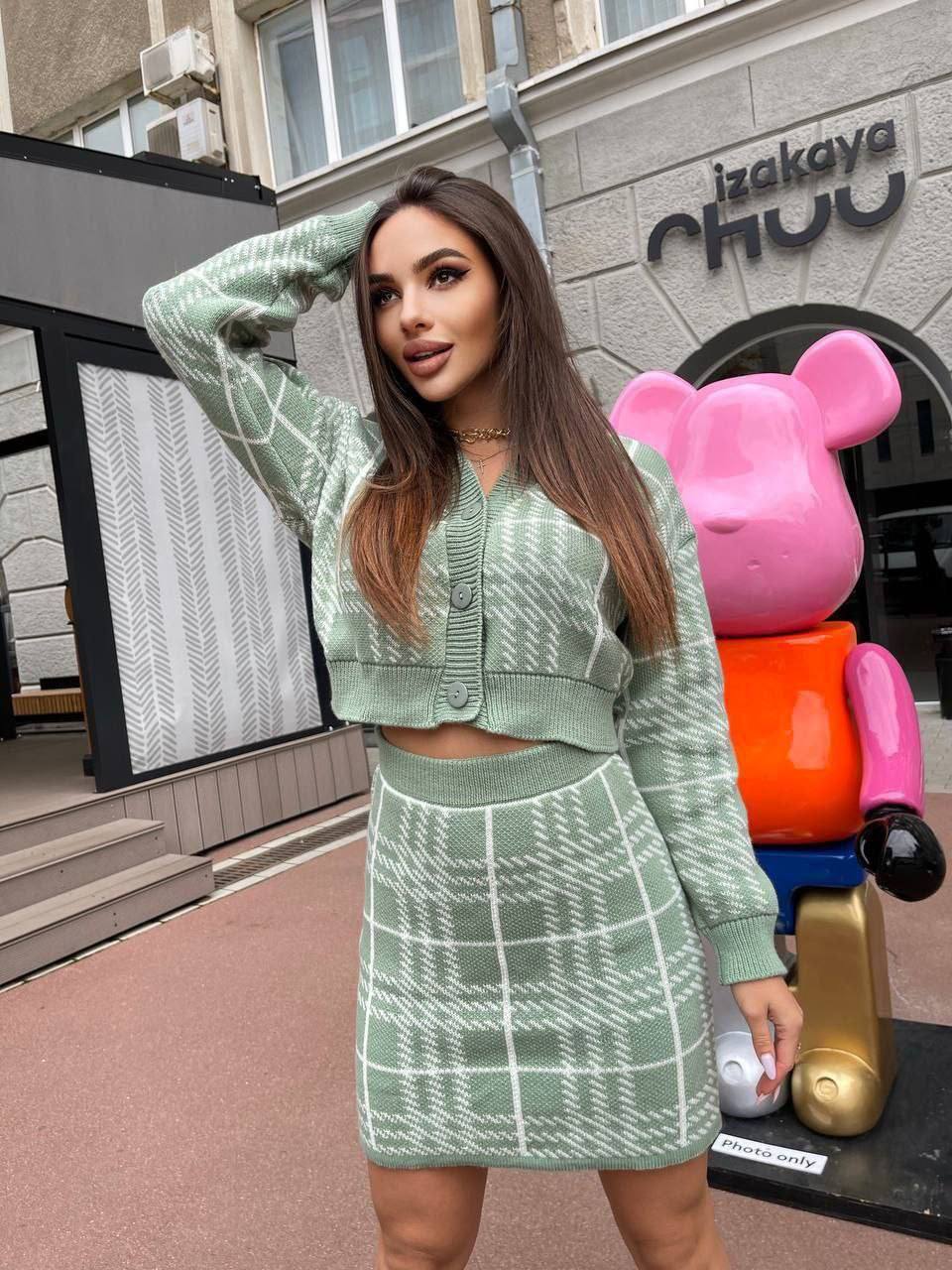 Woman in a green outfit standing in front of a building with a colorful sculpture.