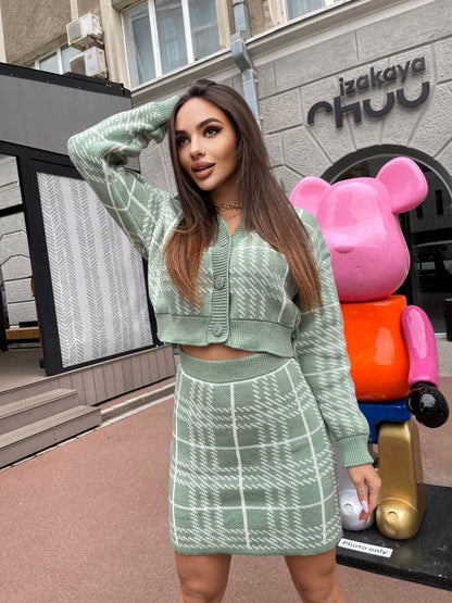 Woman in a green outfit standing in front of a building with a colorful sculpture.