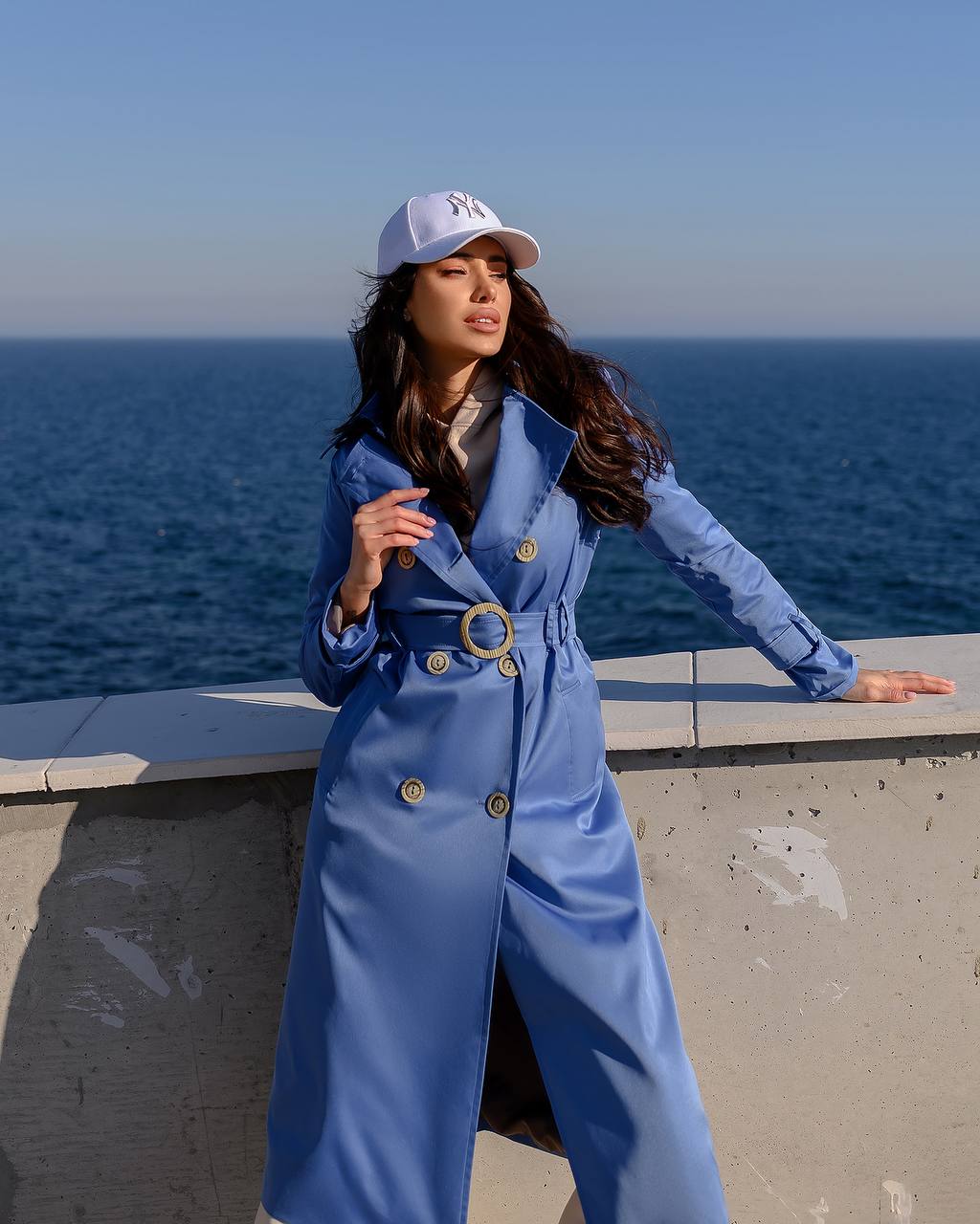 Woman in a blue coat and cap standing by the ocean