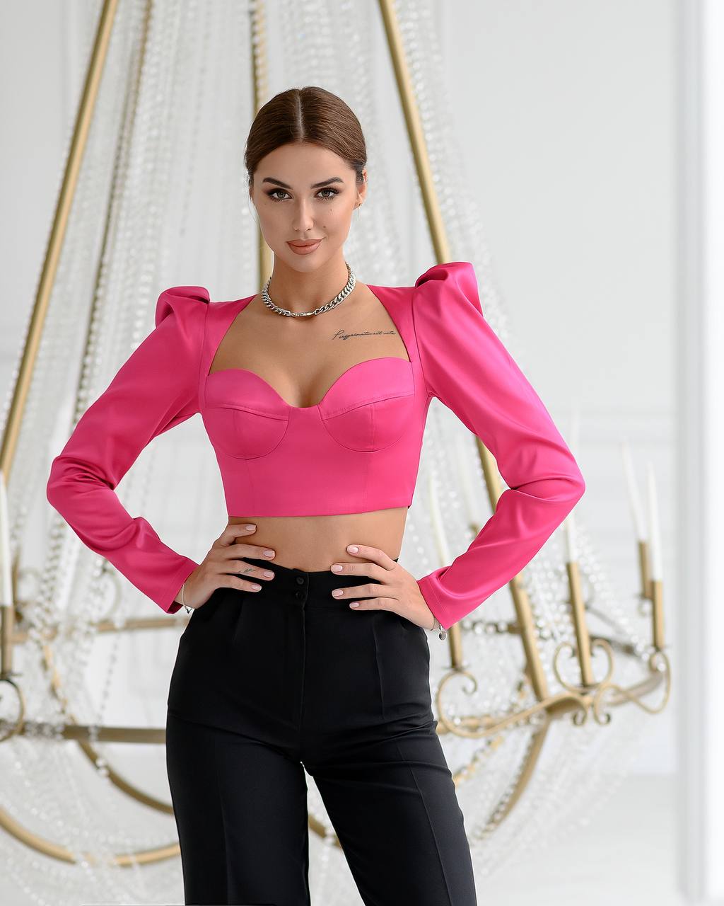 Person wearing a bright pink top with long sleeves and black pants against a decorative background.