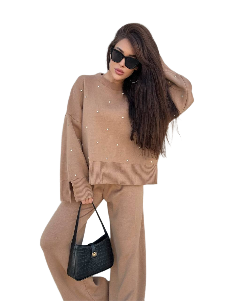 Woman wearing a beige sweater and pants with a black handbag on a white background
