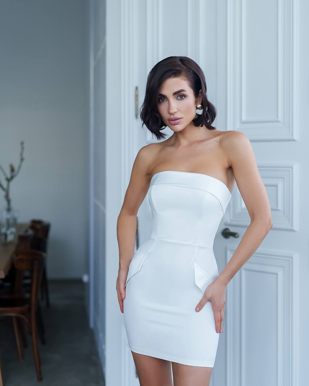 Woman wearing a white strapless dress standing in a room with a neutral background