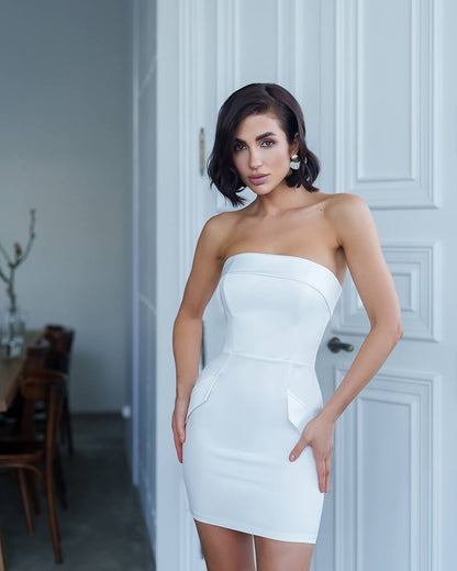 Woman wearing a white strapless dress standing in a room with a neutral background
