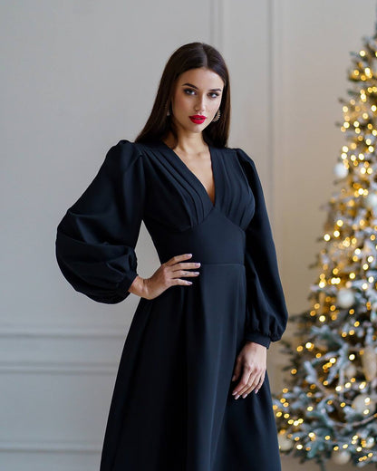 Woman in a black dress standing in front of a decorated Christmas tree.