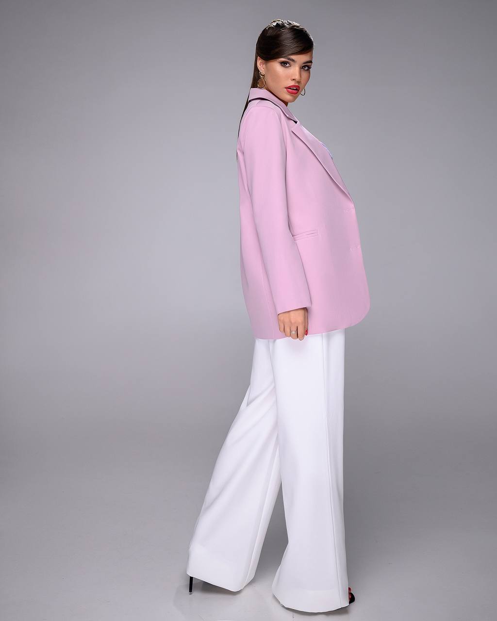 Woman wearing a pink blazer and white pants on a gray background