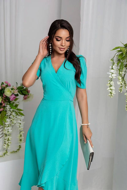 Woman in a teal dress standing against a white background with floral decorations.