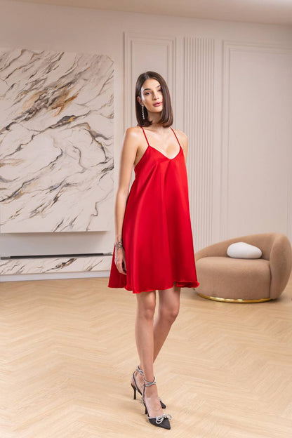 Woman in a red dress standing in a stylish room with marble wall and beige armchair.