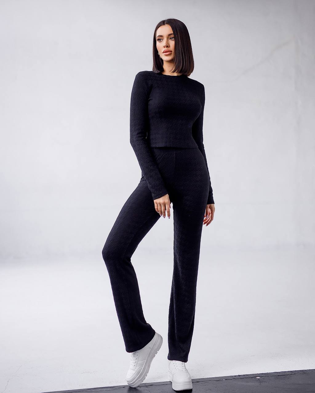 Woman wearing a black outfit with white sneakers on a plain background