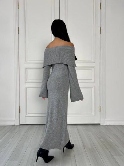 Person wearing a gray off-shoulder outfit standing in a room with white paneled walls.