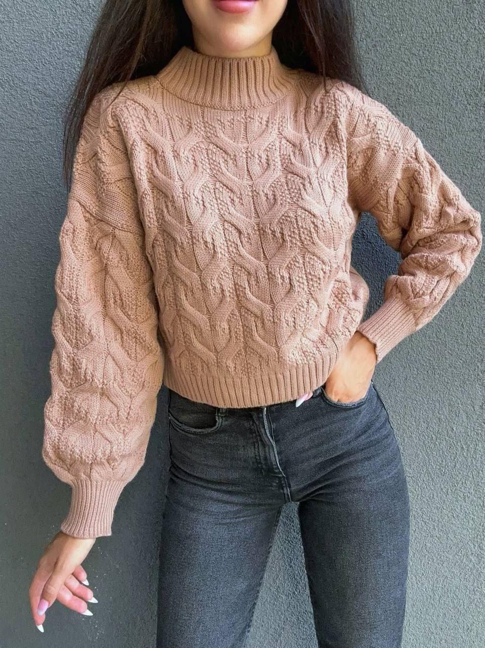 Person wearing a beige cable knit sweater against a gray background