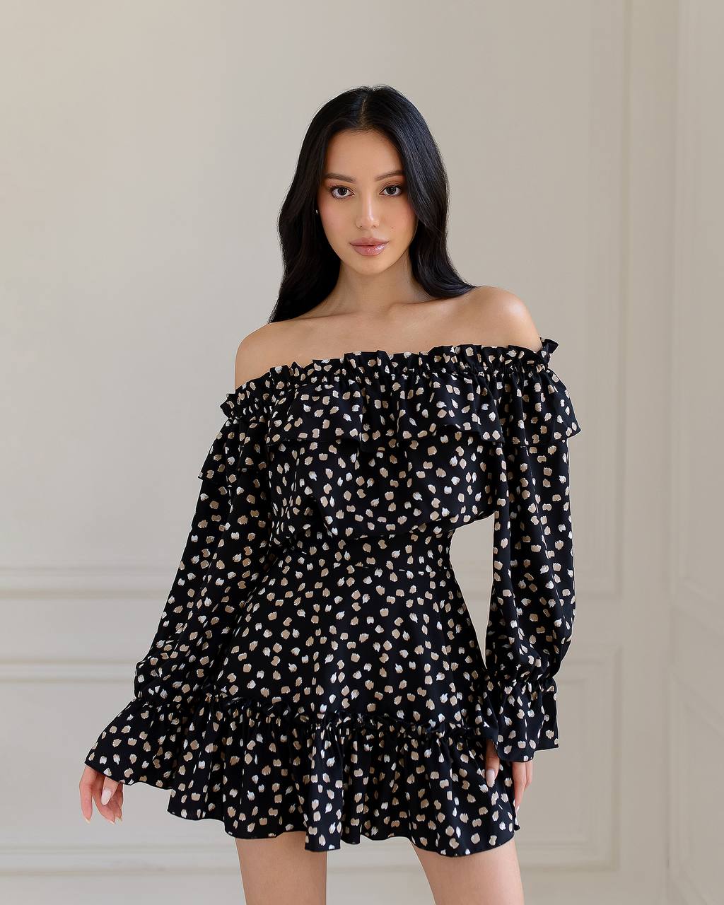 Woman wearing a black off-shoulder dress with white polka dots against a neutral background