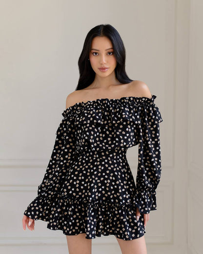 Woman wearing a black off-shoulder dress with white polka dots against a neutral background