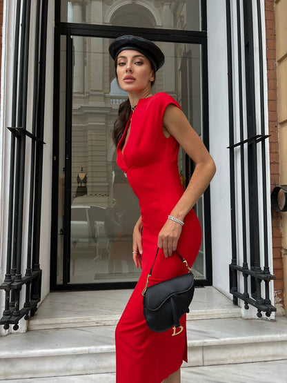 Woman in a red dress and black hat standing in front of a building entrance.