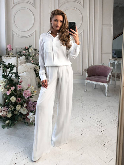 Woman taking a mirror selfie wearing a white outfit in a stylish room with floral decorations.