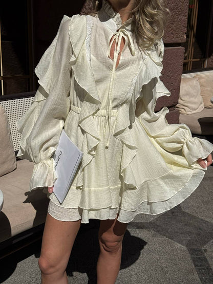 Woman wearing a white ruffled dress holding a book outdoors.