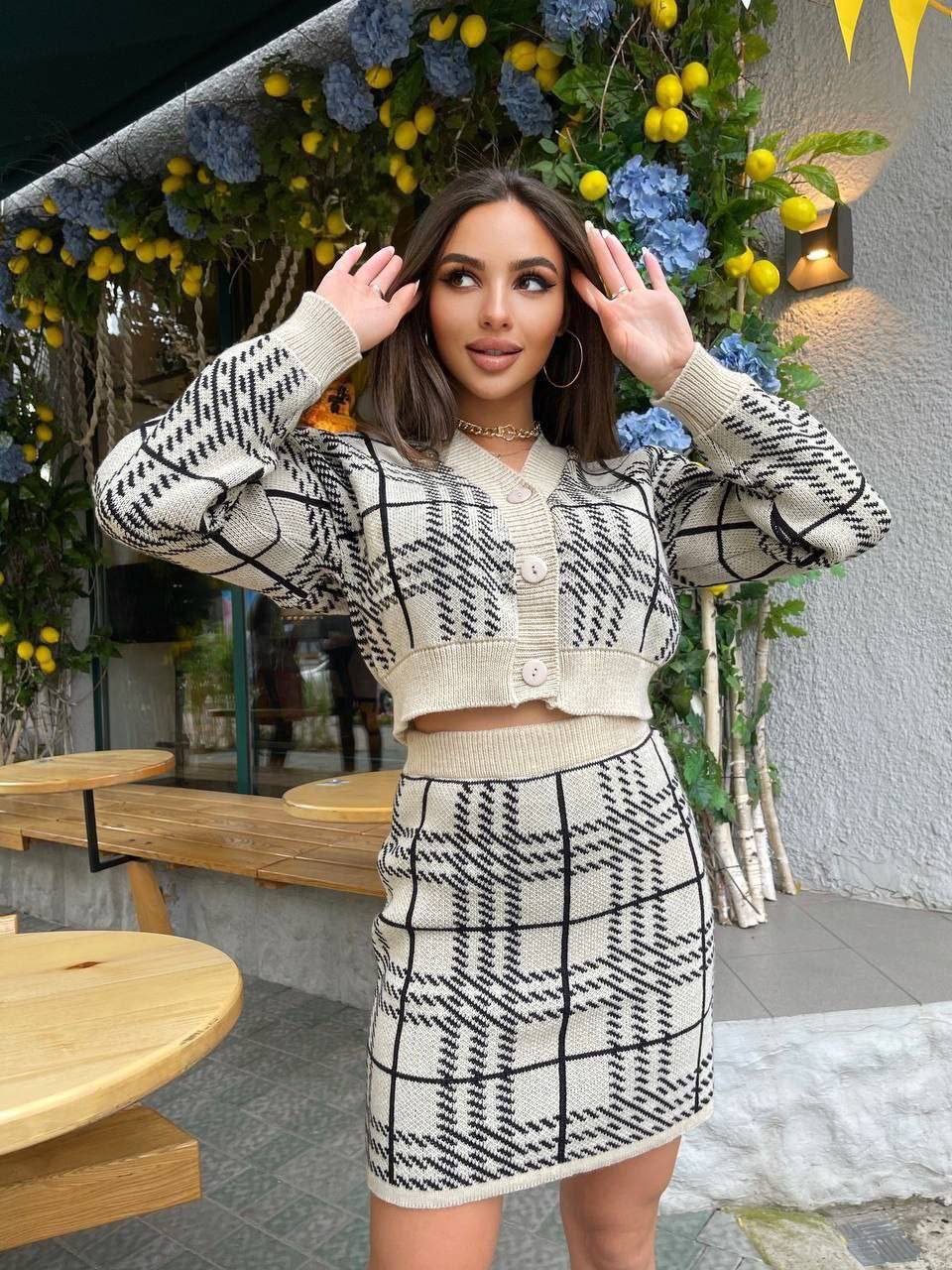Woman in a patterned outfit standing in front of a decorative wall with flowers.