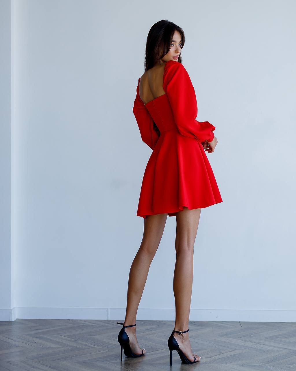 Woman wearing a red dress with a backless design, standing against a white wall.